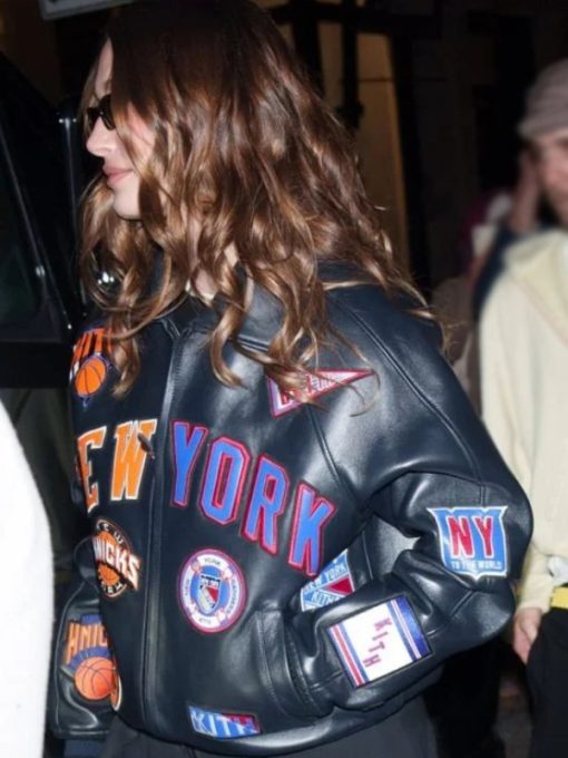 Person wearing a black leather jacket with various patches, including 'New York' and sports team logos.