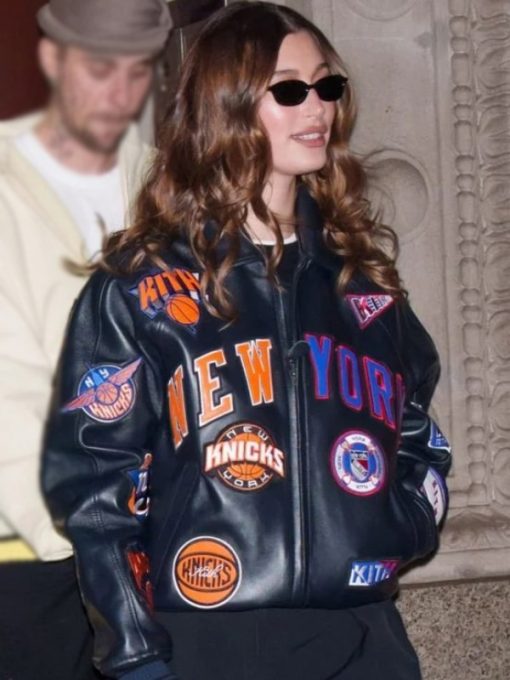 Person wearing a New York Knicks leather jacket with various logos.