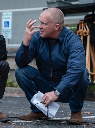 Man in blue shirt and pants squatting on a street holding papers
